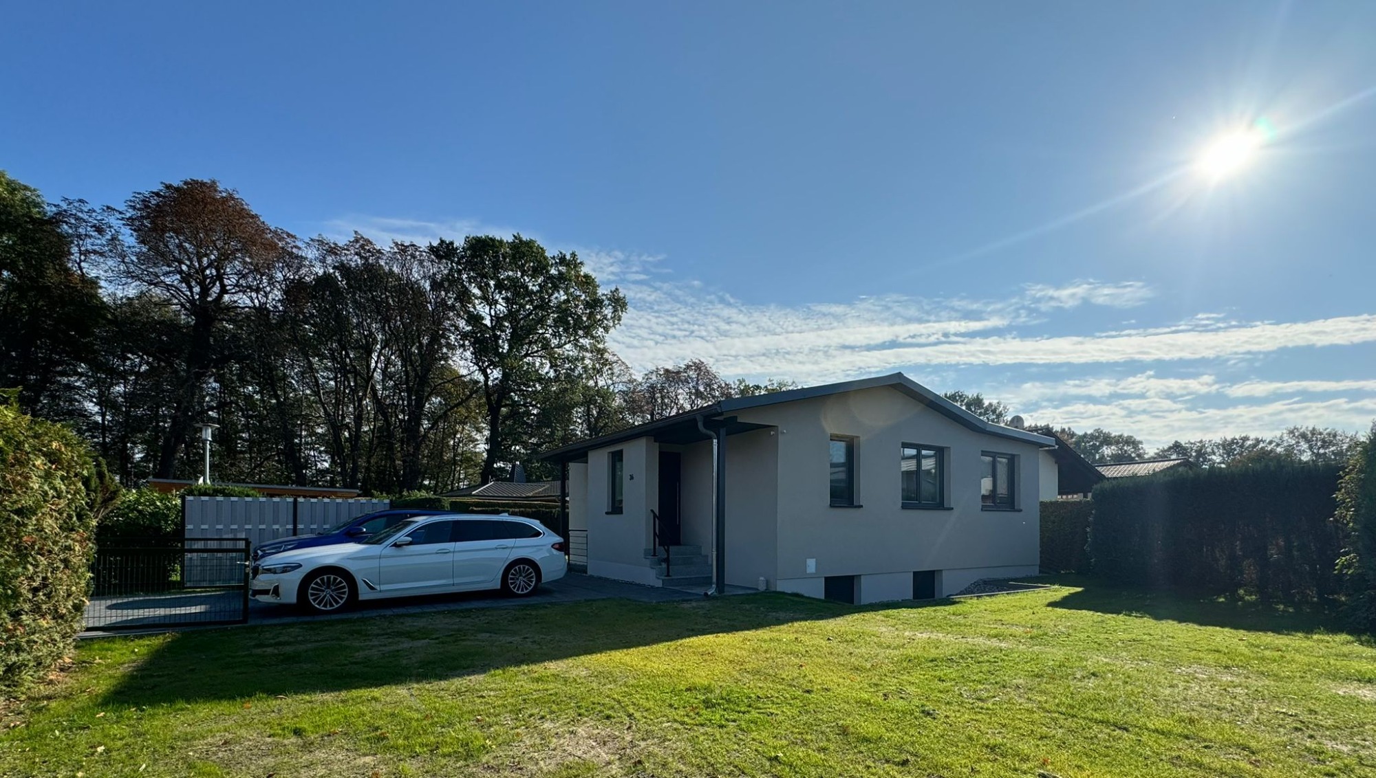 Helles Haus mit Garten und Parkplatz unter klarem Himmel.